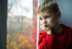 A little boy sitting by the window looking worried