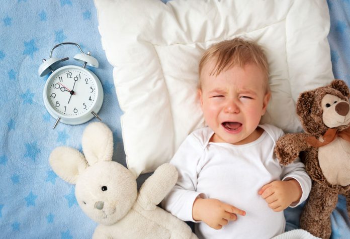 A baby crying at night with an alarm clock and teddy by his side
