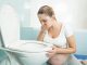 A pregnant woman sitting in a bathroom, feeling sick