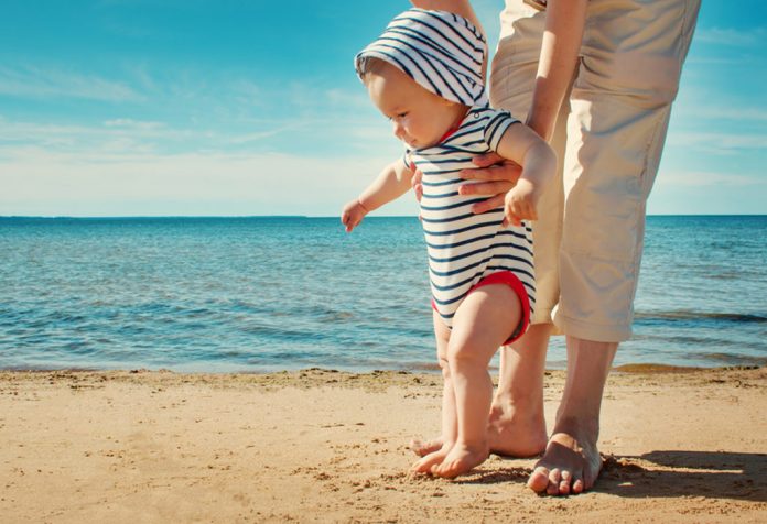 A baby boy walking on the beach with his father